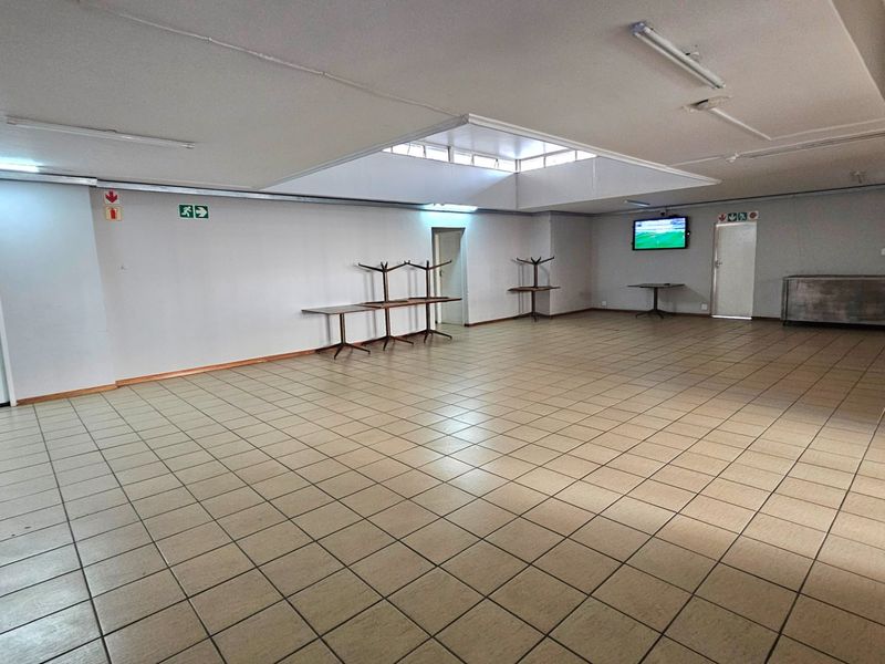 Spacious open-plan commercial area featuring tiled flooring, a central skylight, and functional lighting, suitable for various business or event configurations.