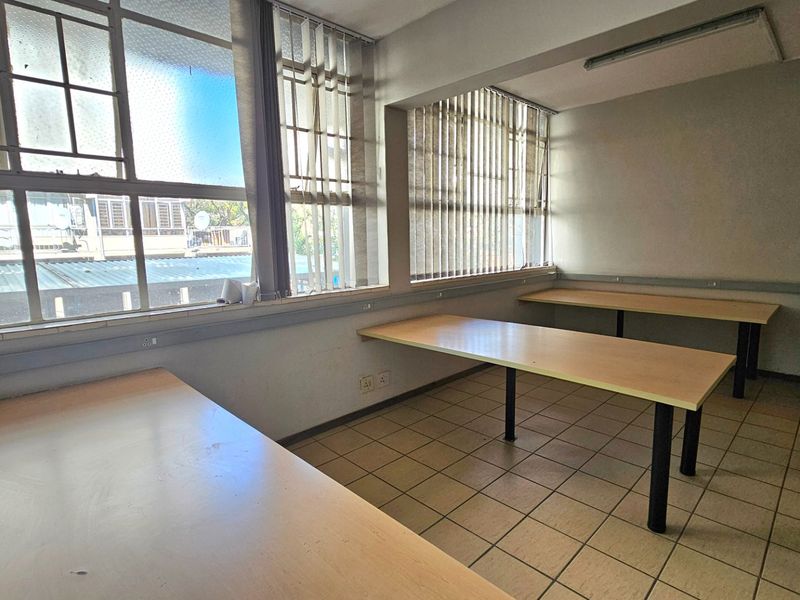 A functional office space featuring large windows with vertical blinds, tiled flooring, and built-in desk surfaces, suitable for a professional work environment.