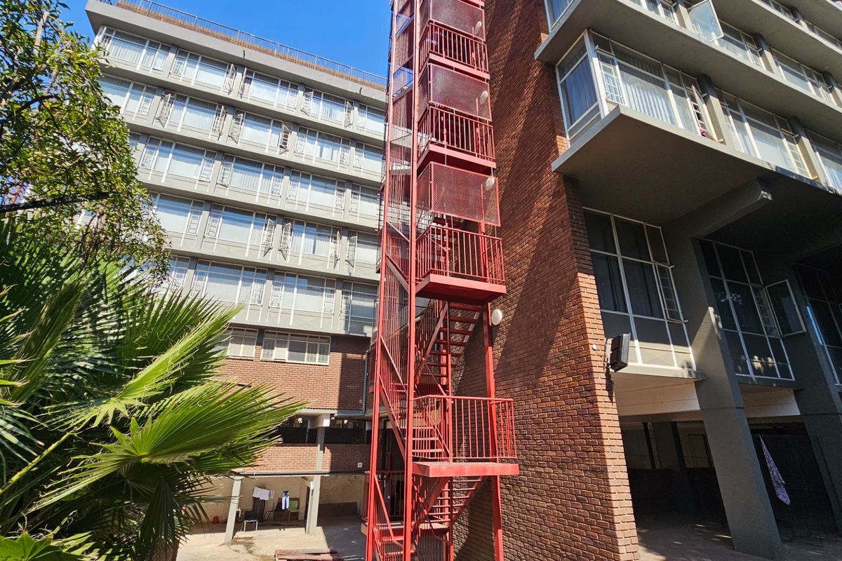 Exterior view of a multi-story commercial building featuring a prominent red steel fire escape staircase and brick facade with multiple window levels.
