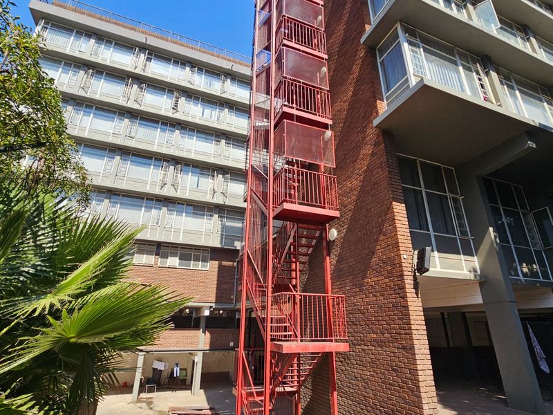Exterior view of a multi-story commercial building featuring a prominent red steel fire escape staircase and brick facade with multiple window levels.