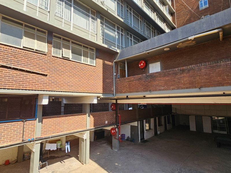 Rear exterior view of a commercial building featuring brick facade, concrete structural elements, and exposed utility piping in a courtyard area.