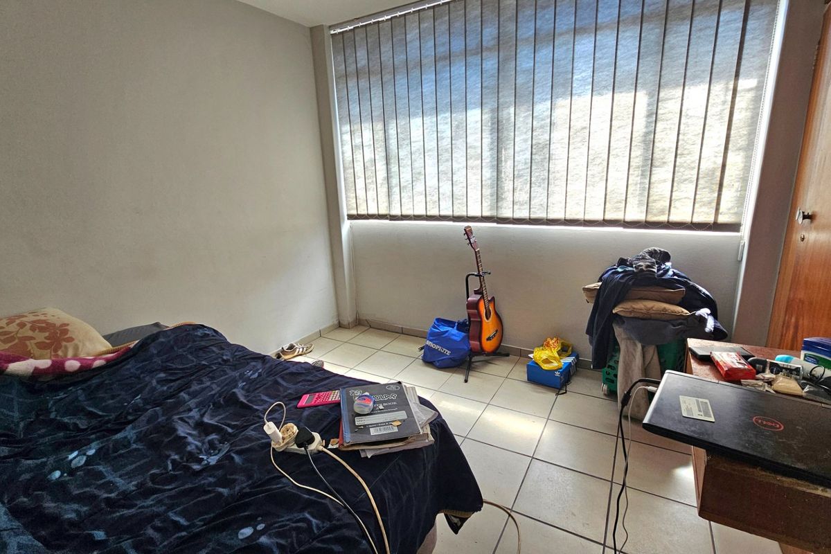 A functional bedroom featuring ceramic floor tiles and large windows with vertical blinds, providing natural light and a neutral base for customization.