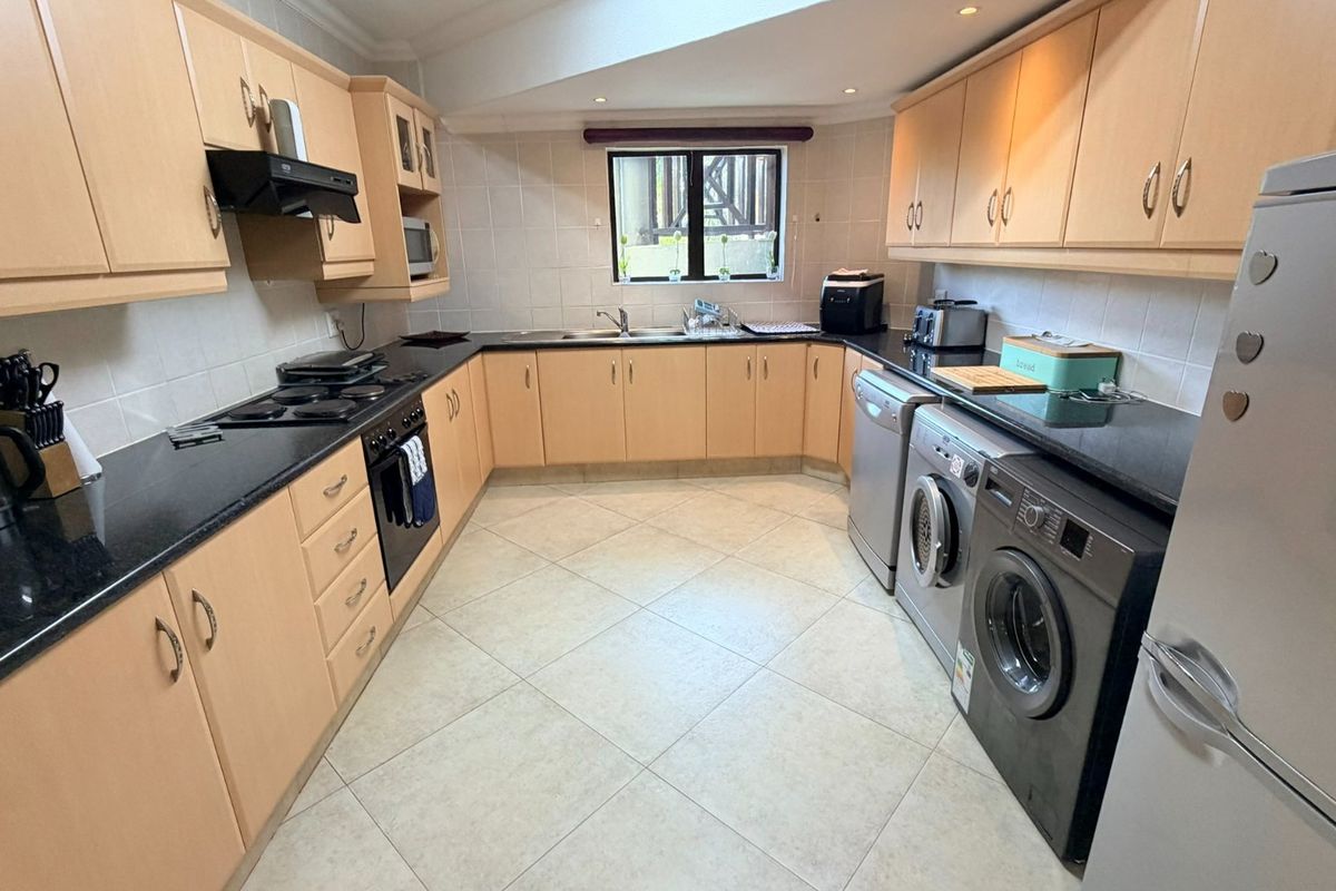 A functional U-shaped kitchen featuring light wood cabinetry, dark granite countertops, tiled backsplash, and integrated appliances with ample storage space.