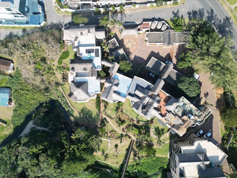 An aerial view of the property showcasing the extensive layout, thatched roof structures, solar panels, swimming pool, and surrounding landscaped gardens.