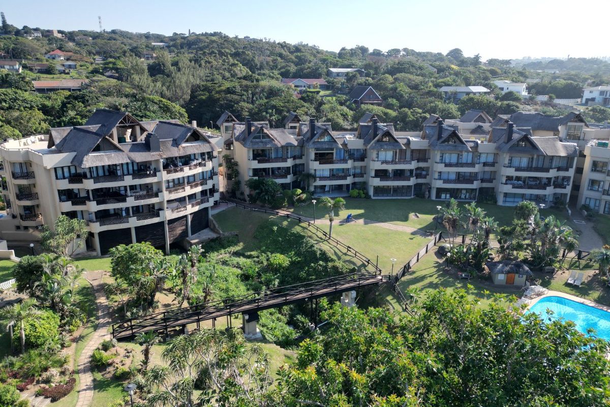Aerial view of a residential apartment complex featuring landscaped gardens, a swimming pool, and a pedestrian bridge connecting the buildings.