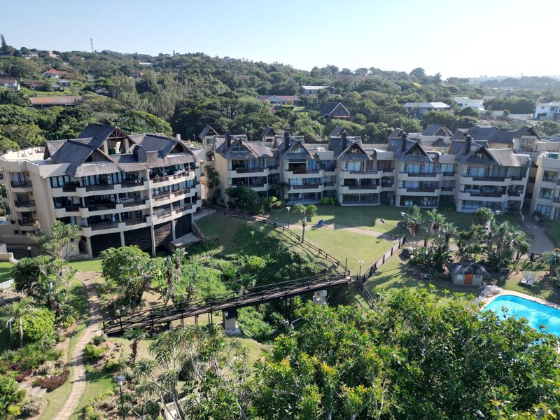 Aerial view of a residential apartment complex featuring landscaped gardens, a swimming pool, and a pedestrian bridge connecting the buildings.