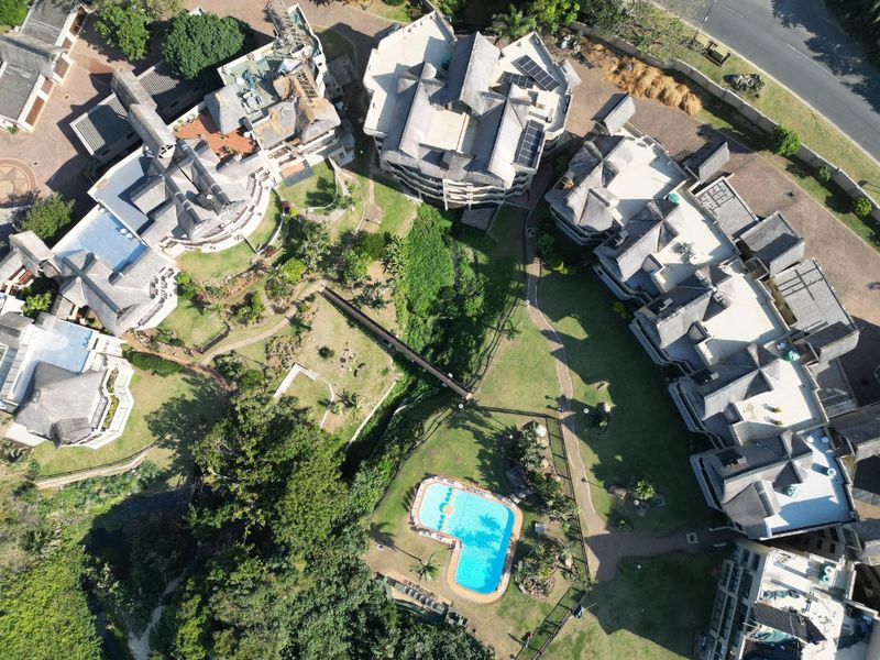 Aerial view of an apartment complex featuring multiple buildings with thatched roofs, landscaped grounds, and a central swimming pool.