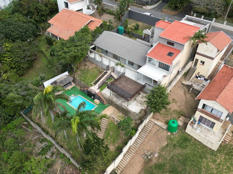 Aerial view of the property featuring a swimming pool, raised timber deck, thatched lapa, and tiered garden areas with retaining walls.