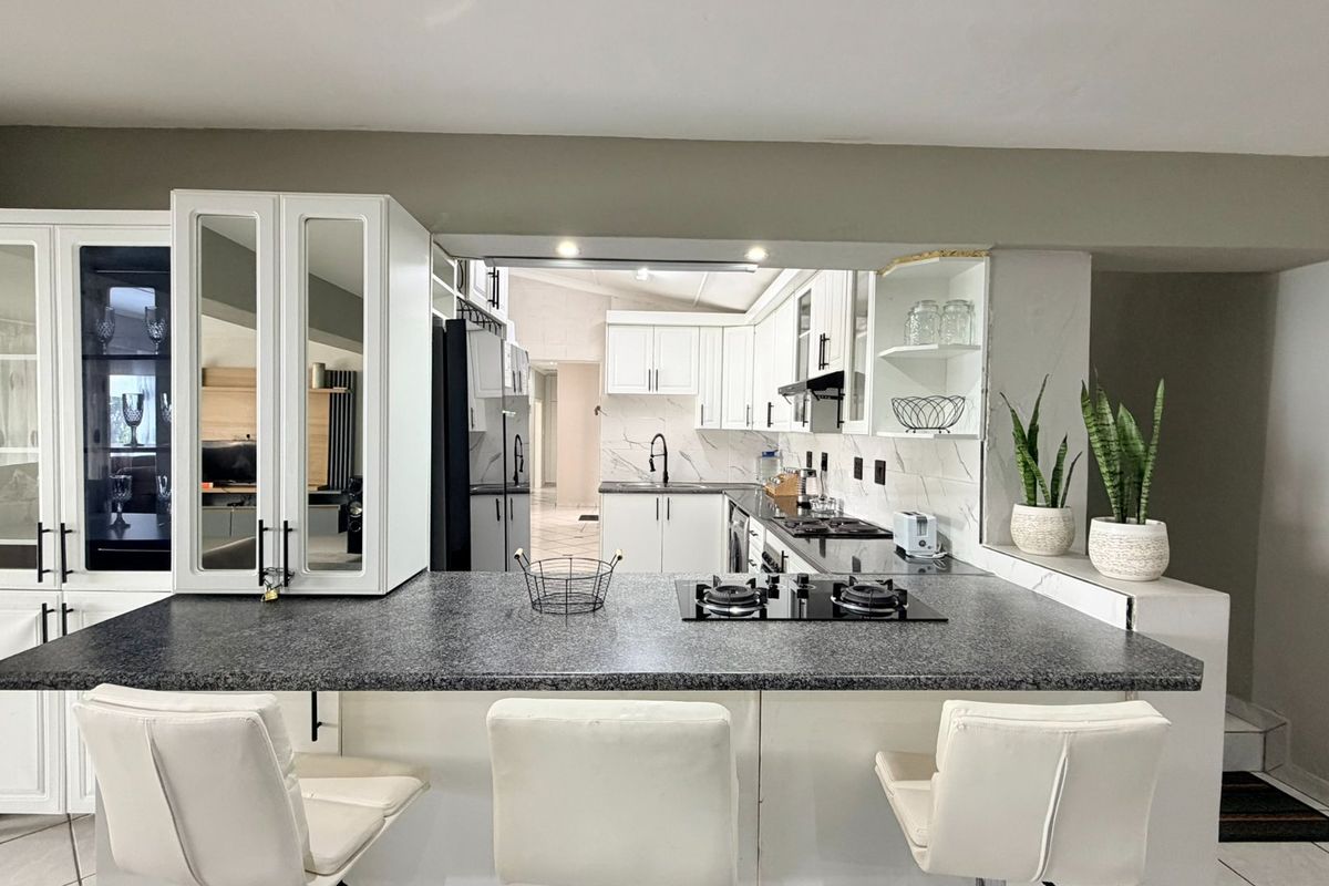 Modern kitchen featuring white cabinetry, stone countertops, a breakfast bar with an integrated gas hob, and glass-fronted display units.