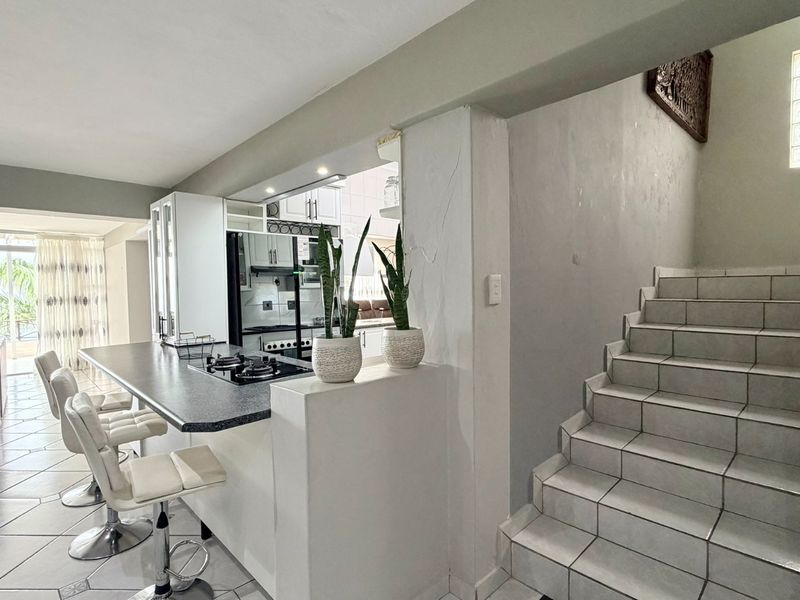 Open plan living area featuring a breakfast bar with integrated gas hob, tiled flooring, and a tiled staircase leading to the upper level.