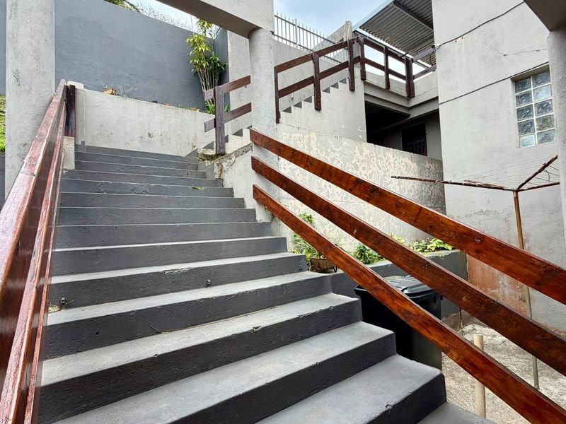 Exterior concrete staircase with timber handrails leading to an upper level, featuring grey painted retaining walls and a glass block window.