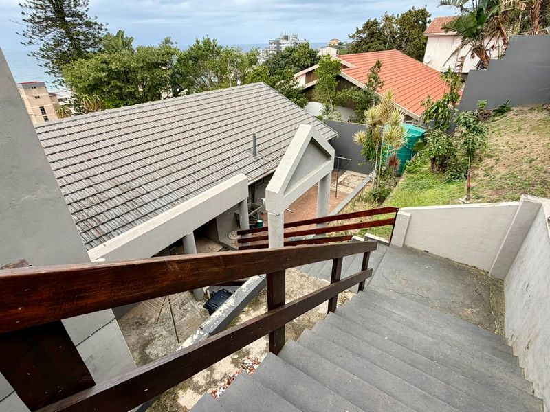 An elevated view of the rear exterior, featuring a concrete staircase with wooden handrails leading down to a paved patio and garden area.