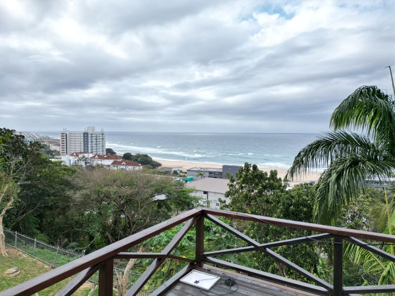 Elevated coastal view overlooking the beach, ocean, and surrounding neighborhood, captured from a wooden deck.