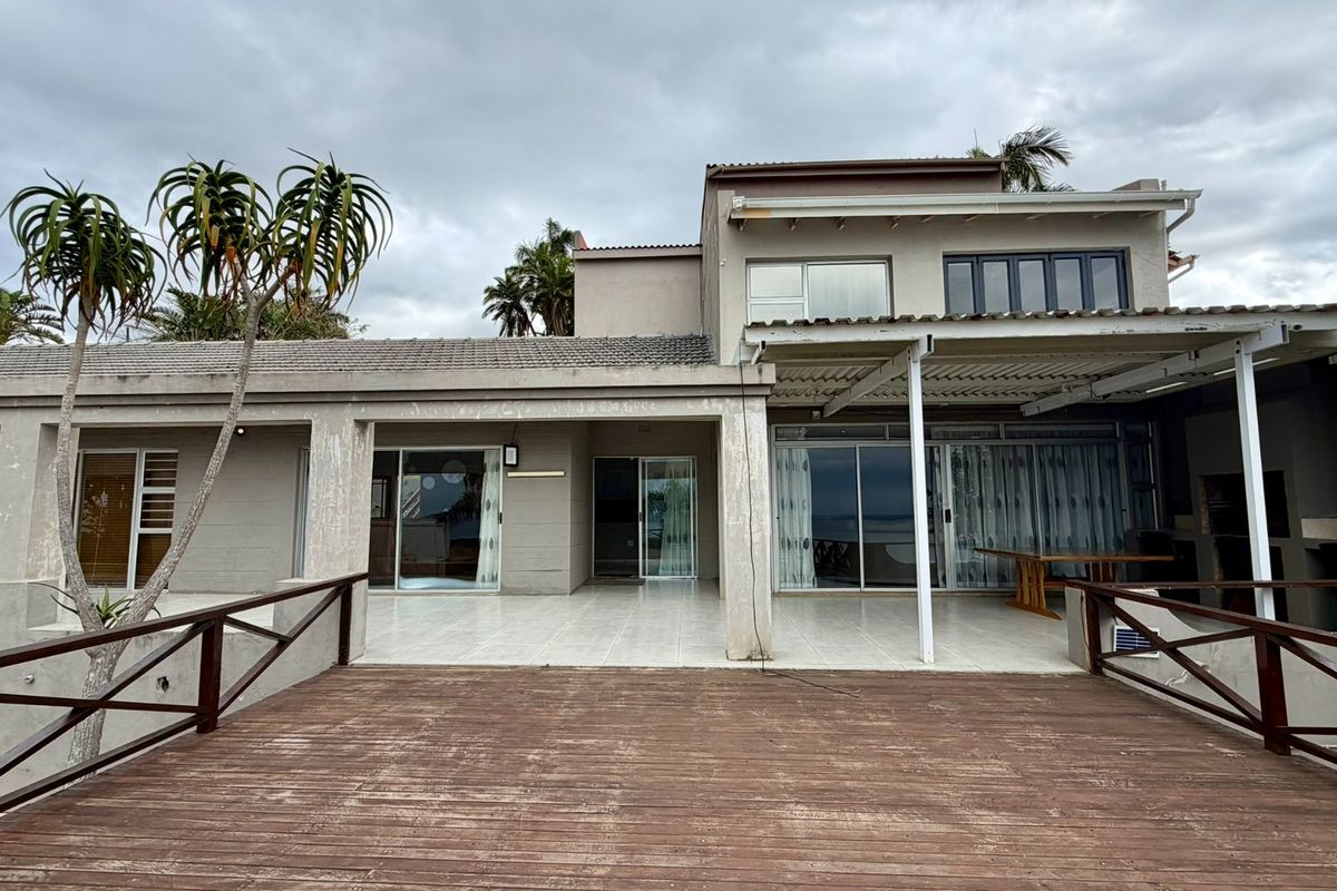 Rear view of the house featuring a spacious tiled patio, a wooden deck, and multiple sliding glass doors providing access to the interior.