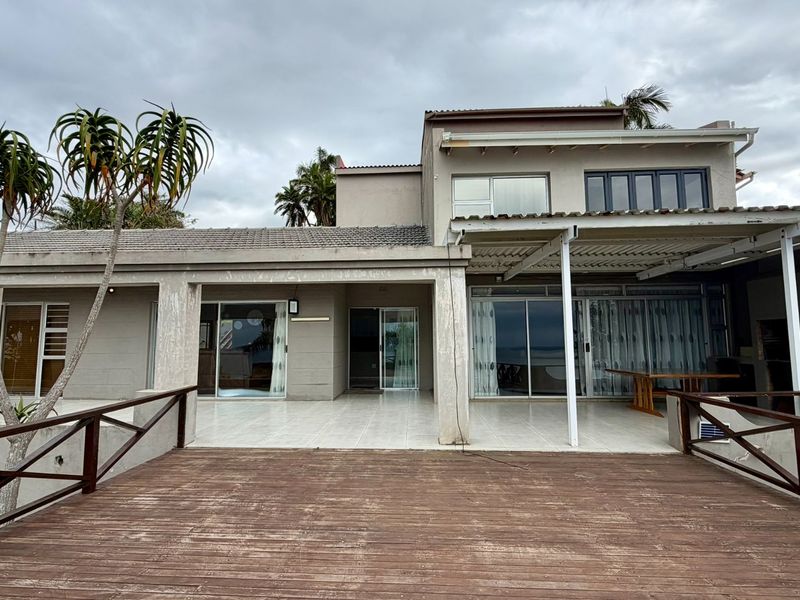 Rear view of the house featuring a spacious tiled patio, a wooden deck, and multiple sliding glass doors providing access to the interior.