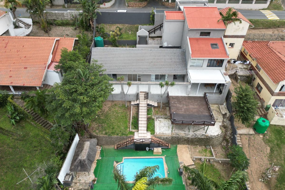 Aerial view of a multi-level residential property featuring a swimming pool, timber deck, thatched lapa, and tiered garden areas.