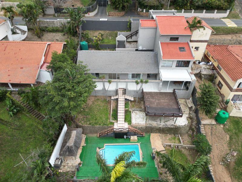 Aerial view of a multi-level residential property featuring a swimming pool, timber deck, thatched lapa, and tiered garden areas.