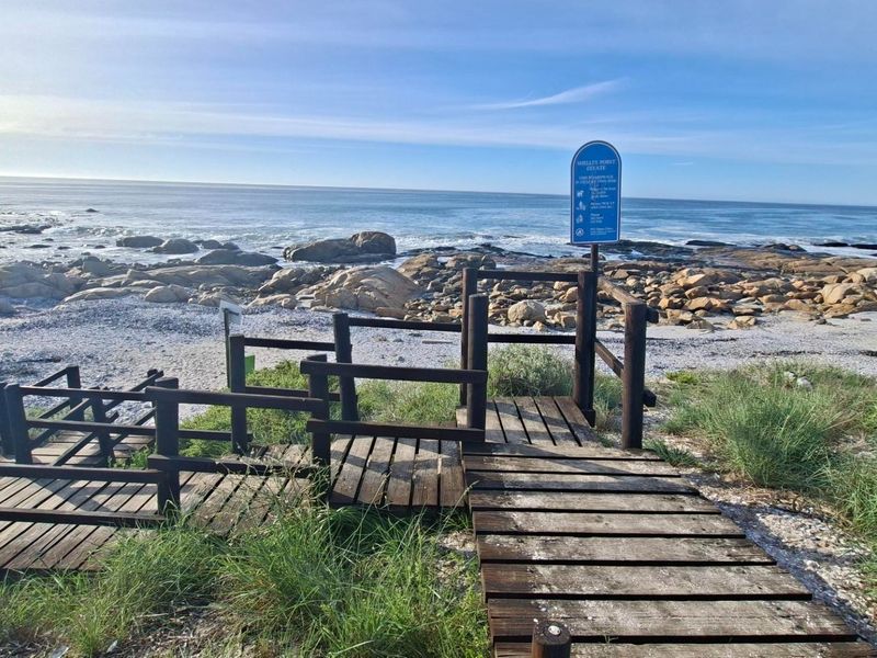A wooden boardwalk providing direct access to the rocky coastline and ocean, featuring weathered timber handrails and a clear view of the sea.