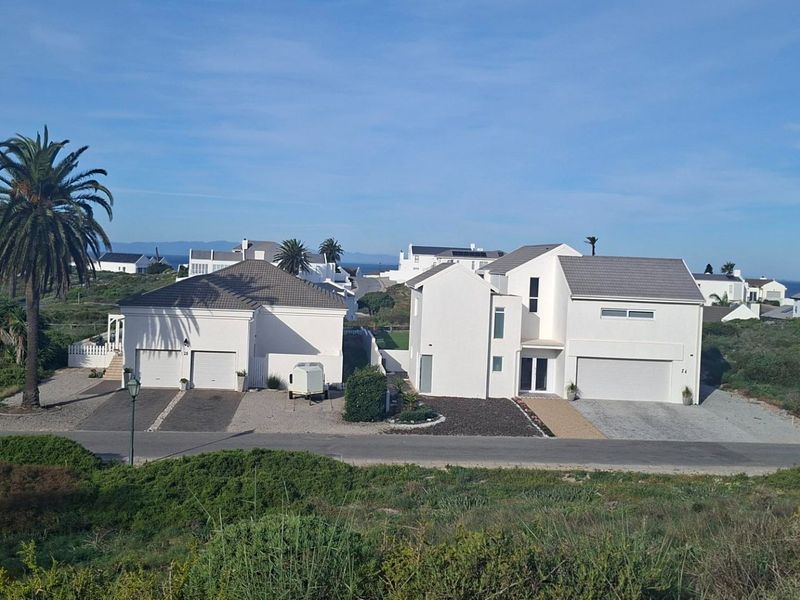 Aerial view of residential properties featuring modern white facades, tiled roofs, and paved driveways in a coastal estate setting.