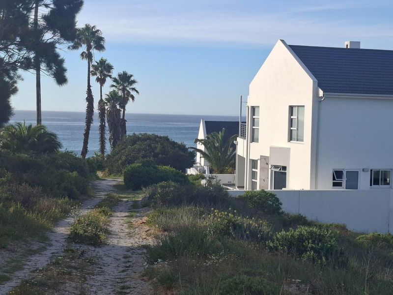 A scenic view of the coastline featuring a natural unpaved path leading towards the ocean, adjacent to a modern residential property.