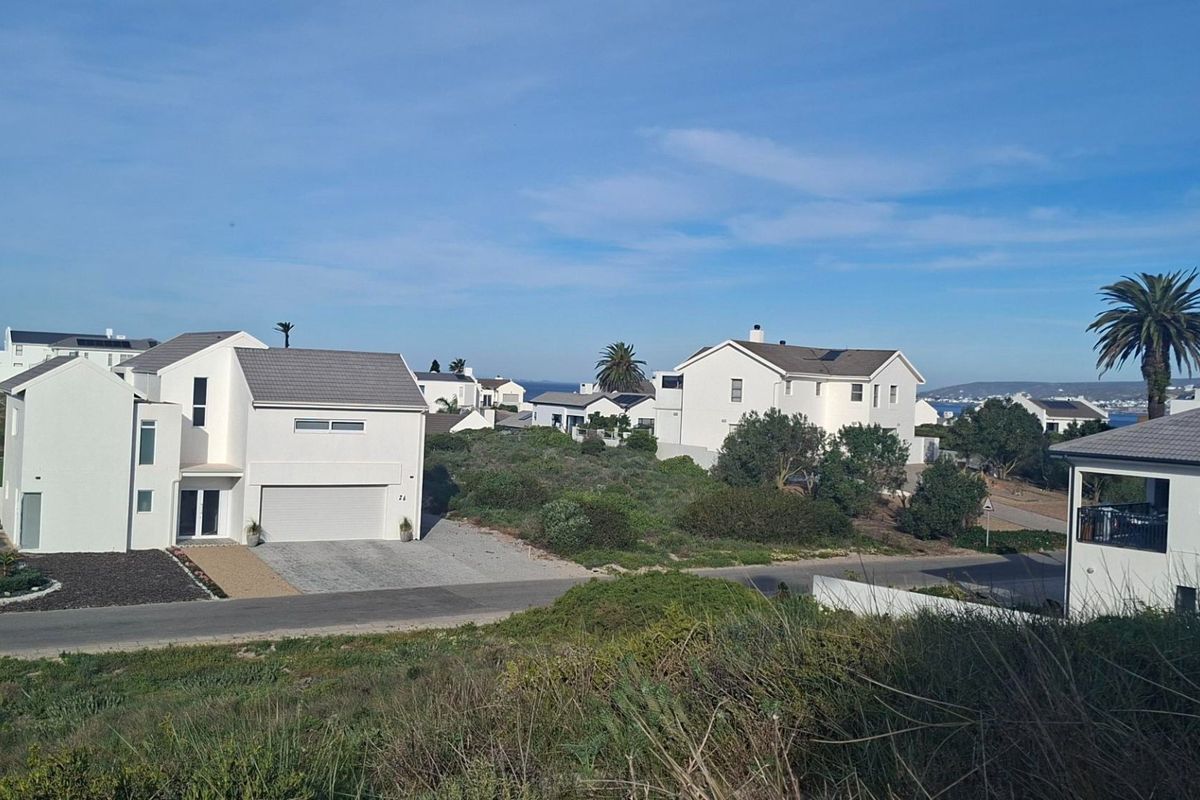 An elevated view of a residential neighborhood featuring modern homes with tiled roofs and paved driveways in a coastal setting.