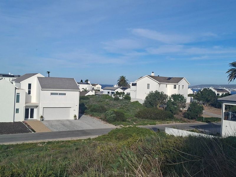 An elevated view of a residential neighborhood featuring modern homes with tiled roofs and paved driveways in a coastal setting.