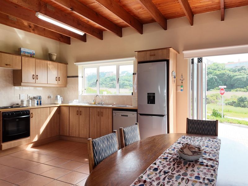 Open-plan kitchen and dining area featuring exposed timber beams, tiled flooring, and bi-fold doors opening to an outdoor view.