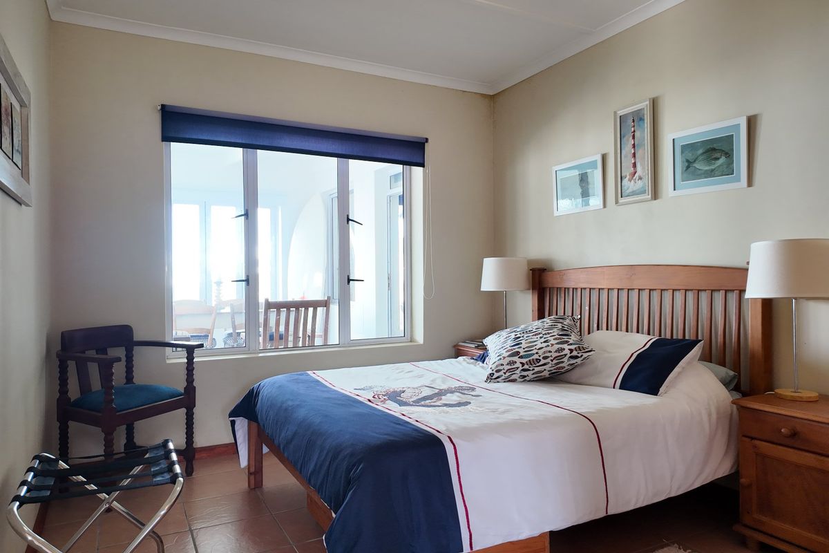 A well-lit bedroom featuring tiled flooring, neutral wall finishes, and a large window with a roller blind, offering a view to an adjacent patio area.