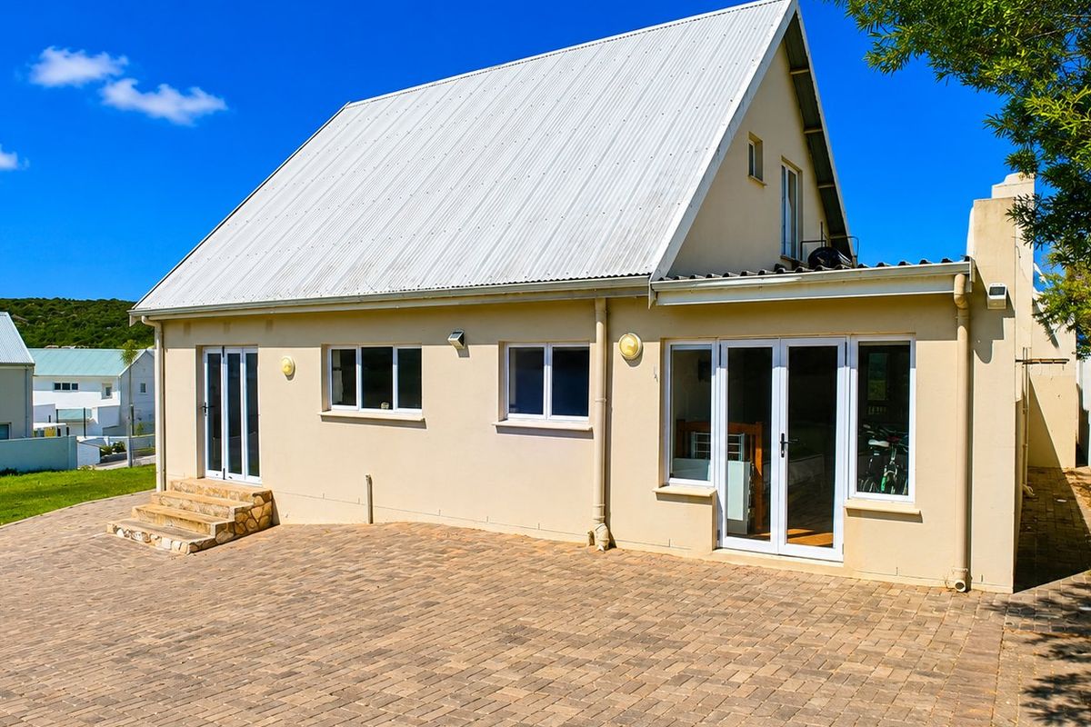 Rear view of the house featuring a paved patio area, stone steps, and white uPVC framed doors and windows under a corrugated metal roof.