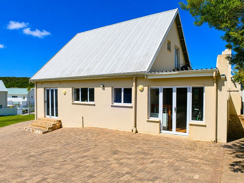 Rear view of the house featuring a paved patio area, stone steps, and white uPVC framed doors and windows under a corrugated metal roof.