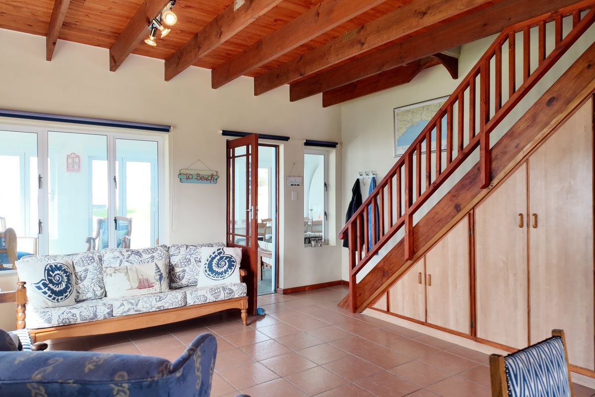 A living room featuring exposed timber ceiling beams, tiled flooring, and a timber staircase with integrated under-stair storage cabinetry.