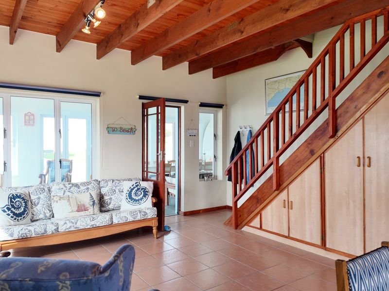 A living room featuring exposed timber ceiling beams, tiled flooring, and a timber staircase with integrated under-stair storage cabinetry.