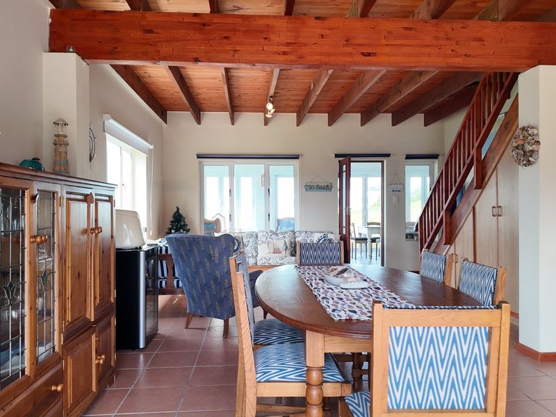 Spacious open-plan living and dining area featuring exposed timber ceiling beams, a wooden staircase, and tiled flooring with access to outdoor space.