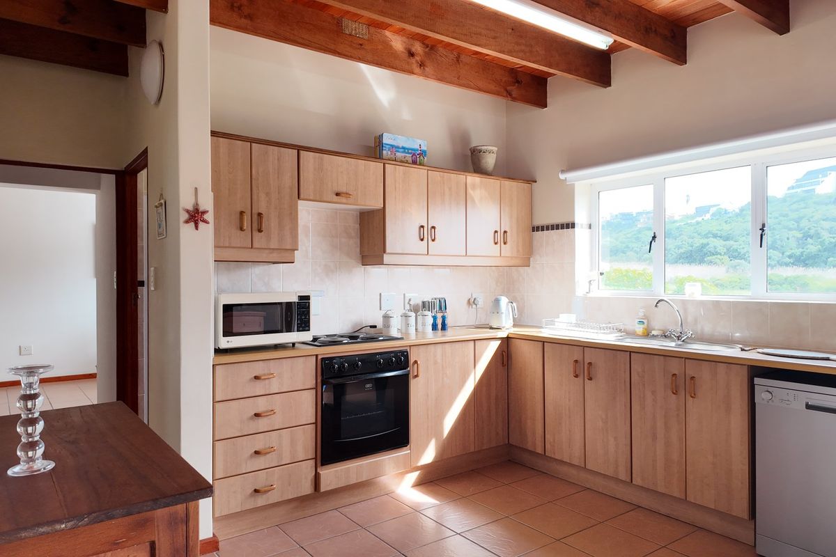 A functional kitchen featuring light wood-finish cabinetry, built-in appliances, tiled surfaces, and exposed timber ceiling beams, offering a warm and practical workspace.