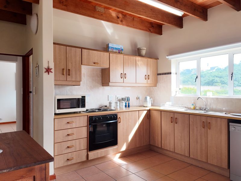 A functional kitchen featuring light wood-finish cabinetry, built-in appliances, tiled surfaces, and exposed timber ceiling beams, offering a warm and practical workspace.