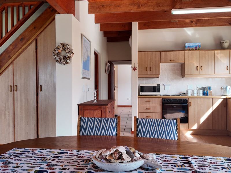Open-plan kitchen and dining area featuring exposed timber beams, a wooden staircase with integrated storage, and functional laminate cabinetry.