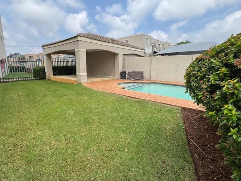 A private backyard featuring a swimming pool, paved surround, and a covered patio area, set within a fenced garden space.