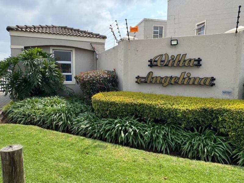 The entrance to Villa Angelina apartment complex, featuring a well-maintained perimeter wall, security fencing, and landscaped garden area.