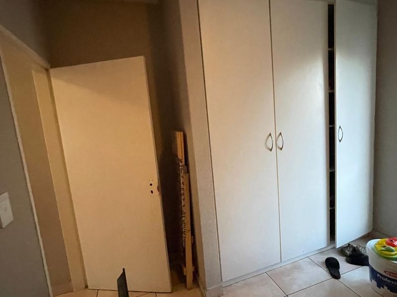 A bedroom featuring built-in cupboards and tiled flooring, currently vacant and requiring minor cosmetic repairs to finishes.