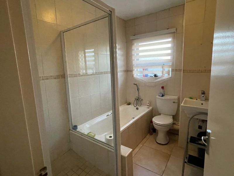 A functional bathroom featuring a combined shower and bathtub, toilet, and wall-mounted basin with neutral tiled finishes throughout.