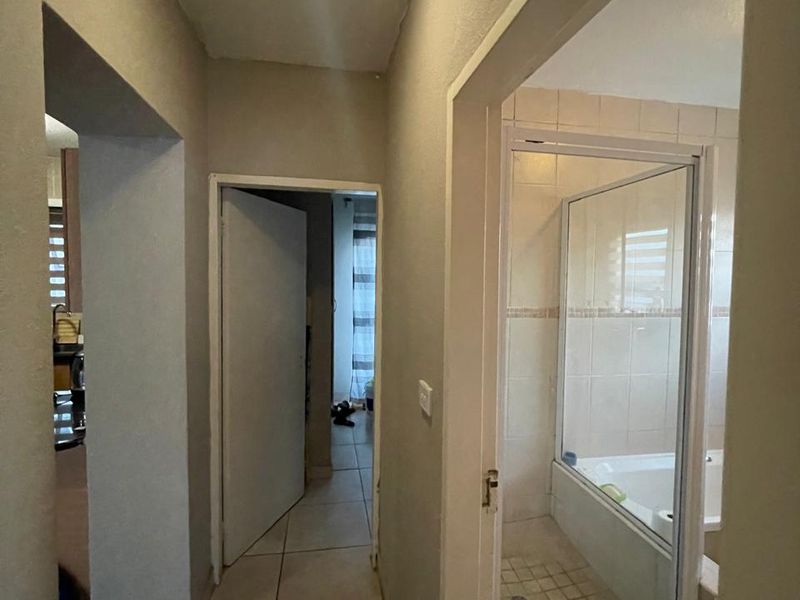 A tiled hallway providing access to a bathroom with a shower and bathtub, featuring neutral wall tones and overhead lighting.