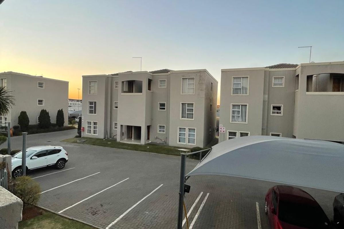 View of the apartment complex exterior featuring paved parking bays with shade sail coverage and multi-story residential building facades.