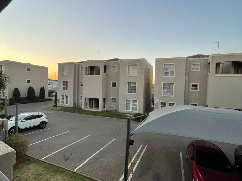 View of the apartment complex exterior featuring paved parking bays with shade sail coverage and multi-story residential building facades.
