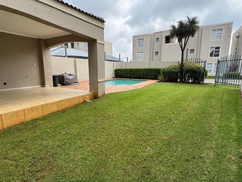 Rear exterior view featuring a covered patio, private swimming pool, paved surround, and a well-maintained lawn area within a secure complex.