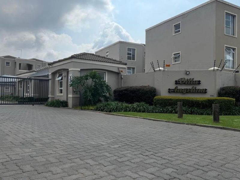 Front entrance view of Villa Angelina apartment complex featuring paved driveway, security gate, and perimeter electric fencing.