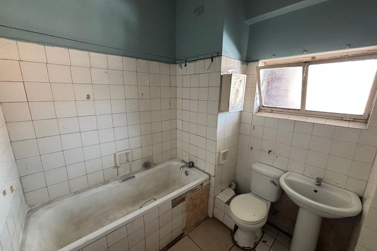 A dated bathroom featuring a standard bathtub, pedestal basin, and toilet, requiring significant renovation and cosmetic updates to improve its condition and functionality.