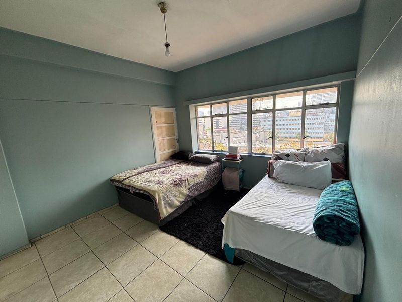 A bedroom featuring tiled flooring and a large window providing natural light and an urban view.