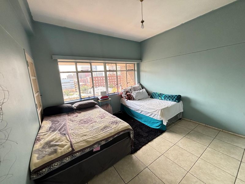 A spacious bedroom featuring tiled flooring, a large window with city views, and built-in storage, offering a functional living space.