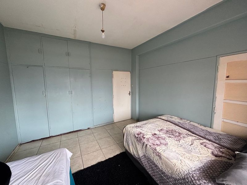 A bedroom featuring built-in cupboards, tiled flooring, and a pendant light. The room shows signs of wear and requires cosmetic updates.
