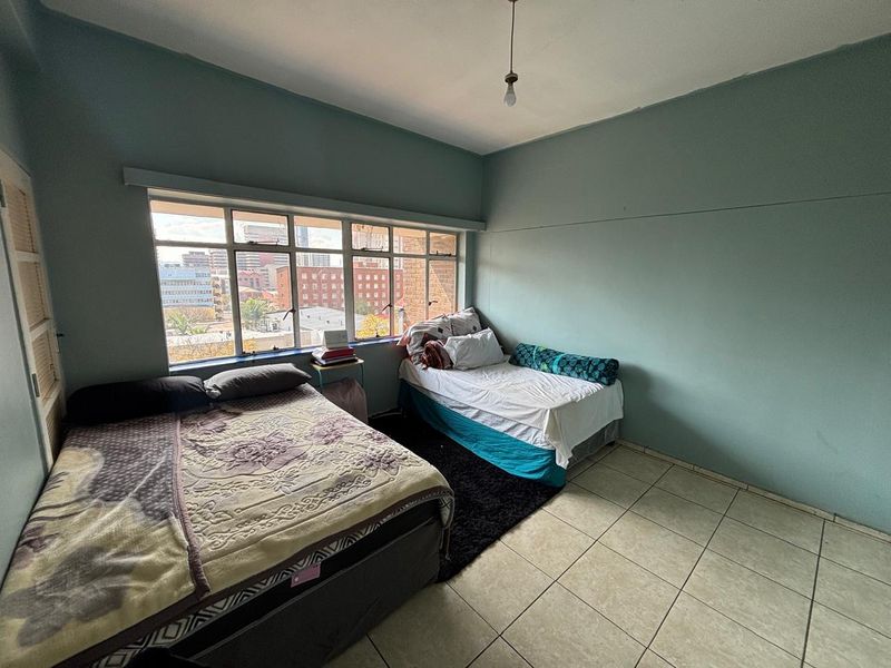 A bedroom featuring large windows with city views, tiled flooring, and built-in storage, offering a functional space with potential for cosmetic updates.